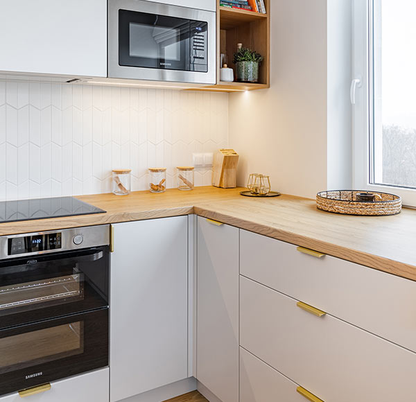 Jasna, funkcjonalna kuchnia w stylu skandynawskim z drewnianym blatem, białymi frontami i złotymi uchwytami.