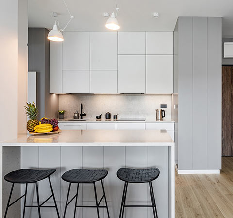 Nowoczesna kuchnia z białą zabudową, wyspą i trzema czarnymi hokerami.