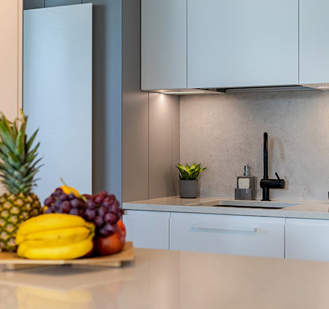 Minimalistyczna kuchnia z czarną baterią, jasnymi frontami i owocami na blacie.